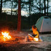 reading a book with lantern in front of fire at beach campsite